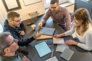 © Schreinerladen Föhren GmbH & Co. KG / Privat/Non-kommerziell Die vier Familienmitglieder Follmann sitzen an einem Tisch und arbeiten zusammen.