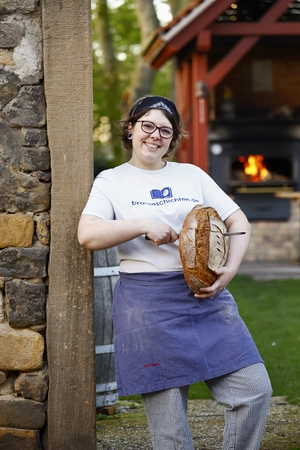 © Melhubach Photographie / Privat/Non-kommerziell Marie Bochmann, Inhaber der Sauerteigbäckerei Brotgeschichten steht mit einem Leib Brot in der Hand vor einem Baum. Sie lächelt freundlich in die Kamera
